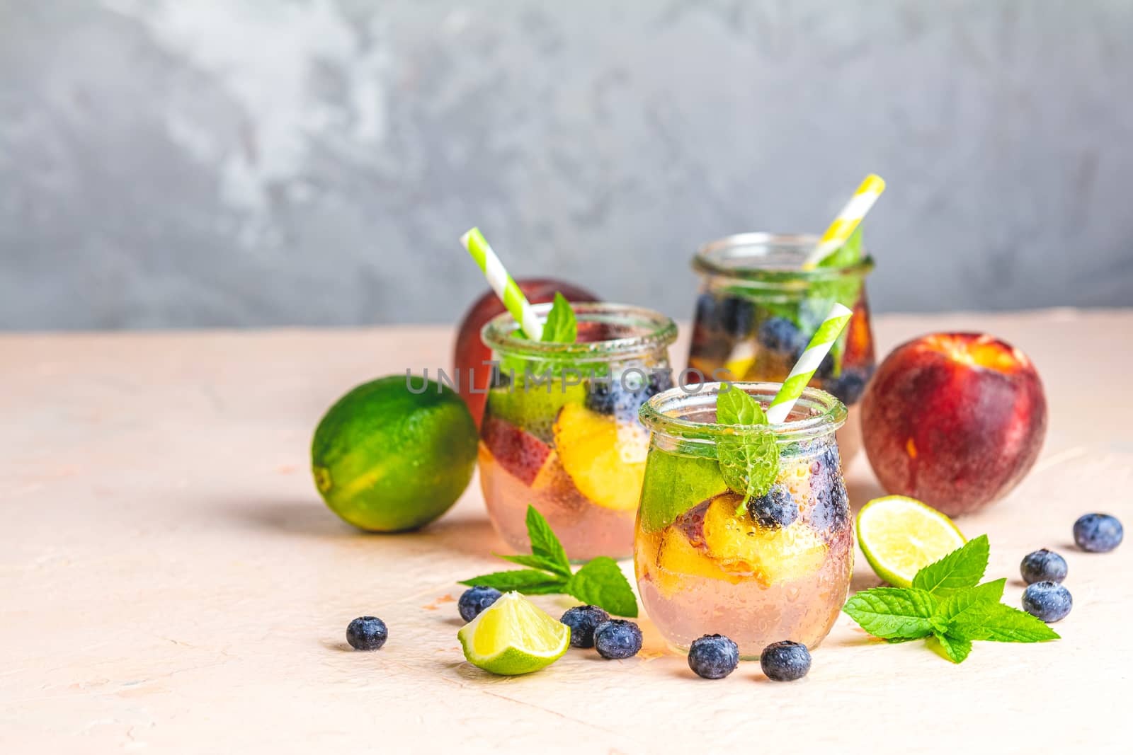 Blueberry and peach infused water, cocktail, lemonade or tea in jar with water drops. Summer iced cold drink with blueberry, lime, peach and mint