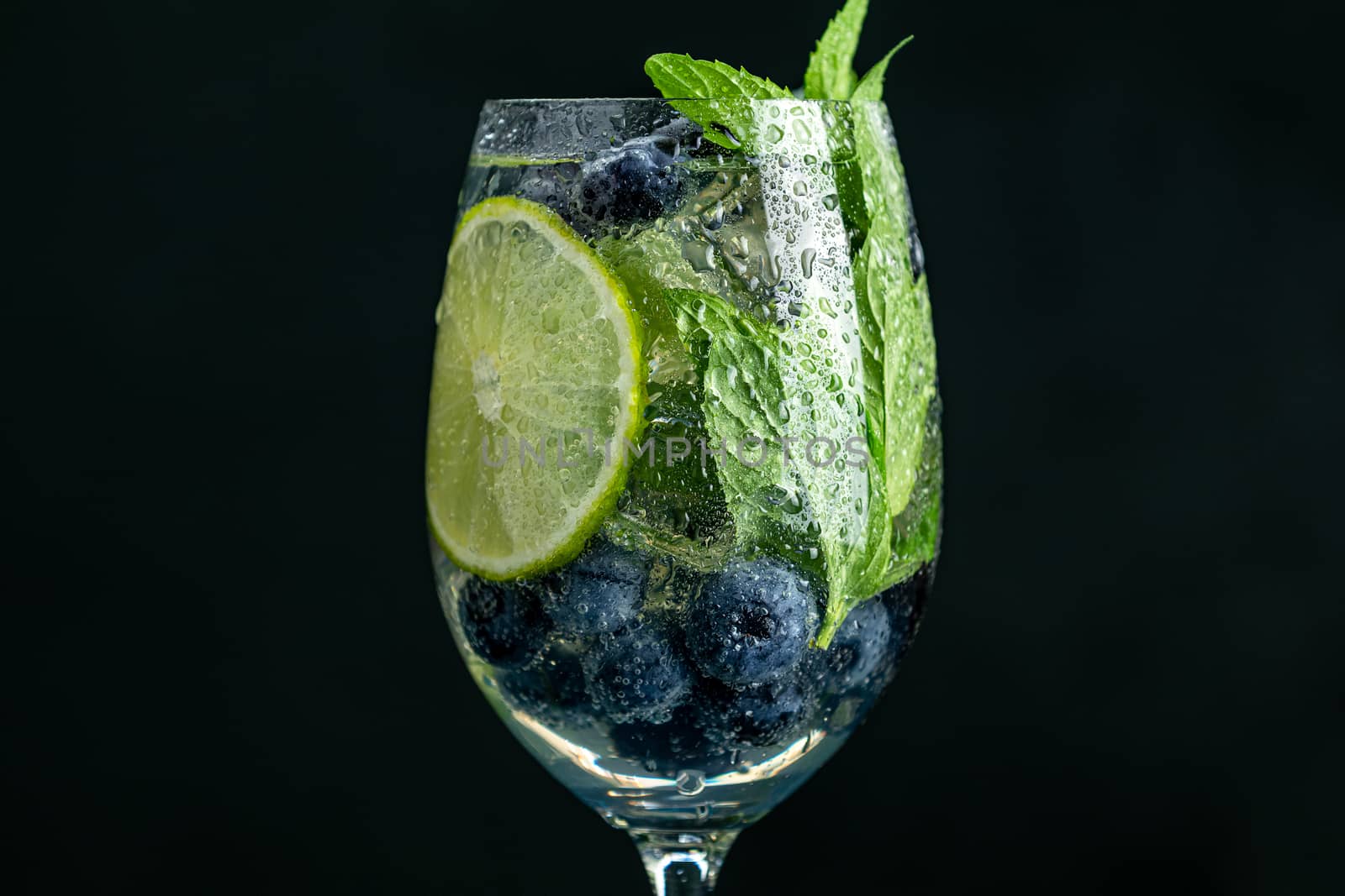 Summer alcoholic cocktail blueberry mojito with rum, mint, lime and ice, close up, dark background, selective focus, copy space