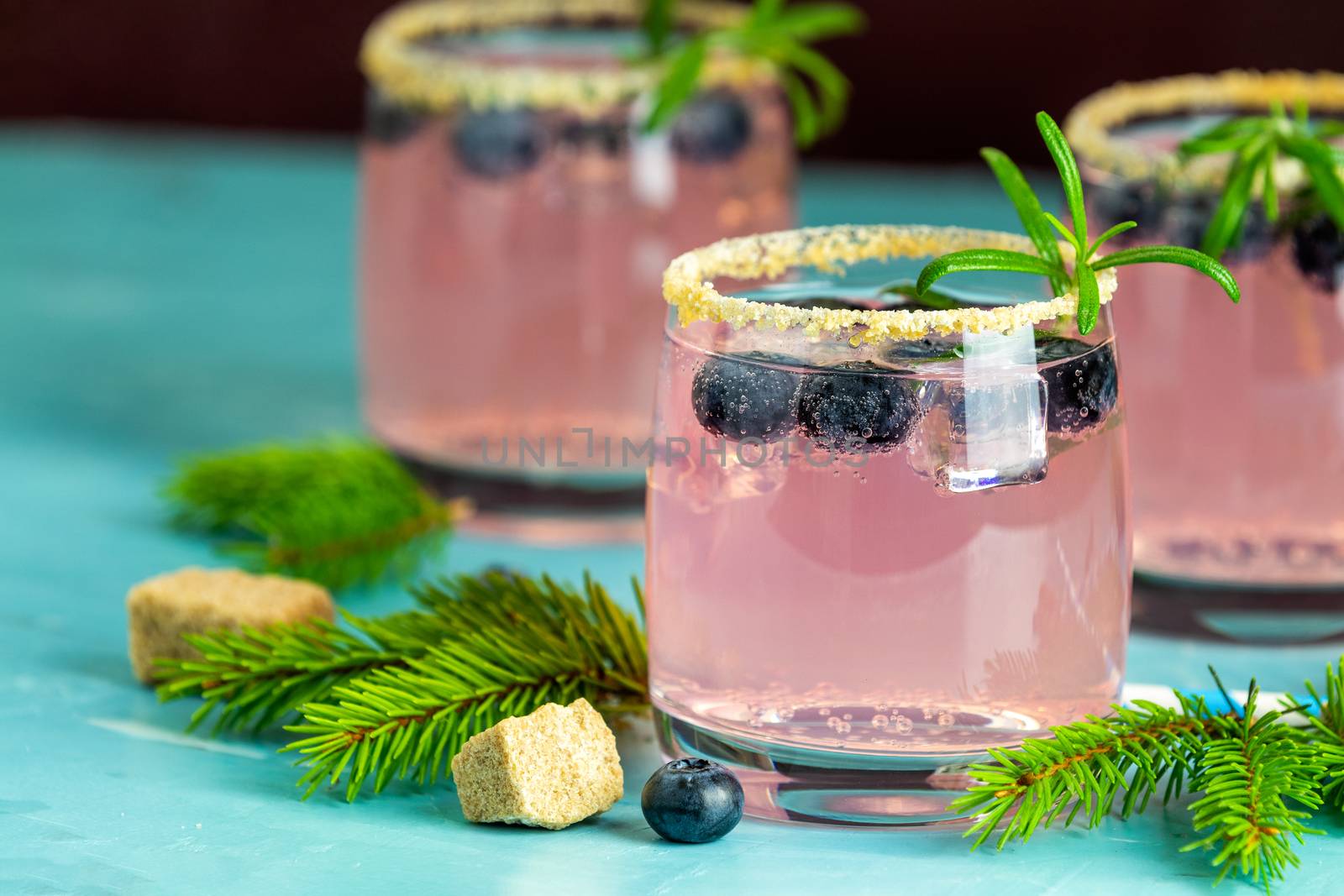 Fresh blueberry cocktail with rosemary and ice in glasses with decorate brown sugar on turquoise surface and black background. Christmas and New Year holiday welcome drink. 