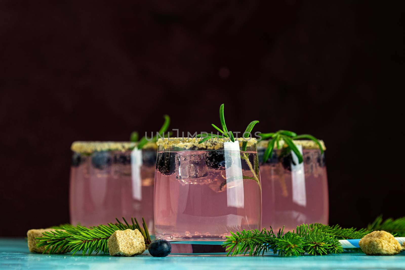Fresh blueberry cocktail with rosemary and ice in glasses with decorate brown sugar on turquoise surface and black background. Christmas and New Year holiday welcome drink. 