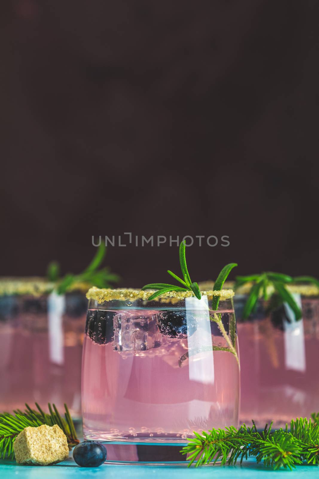 Fresh blueberry cocktail with rosemary and ice in glasses with decorate brown sugar on turquoise surface and black background. Christmas and New Year holiday welcome drink. 