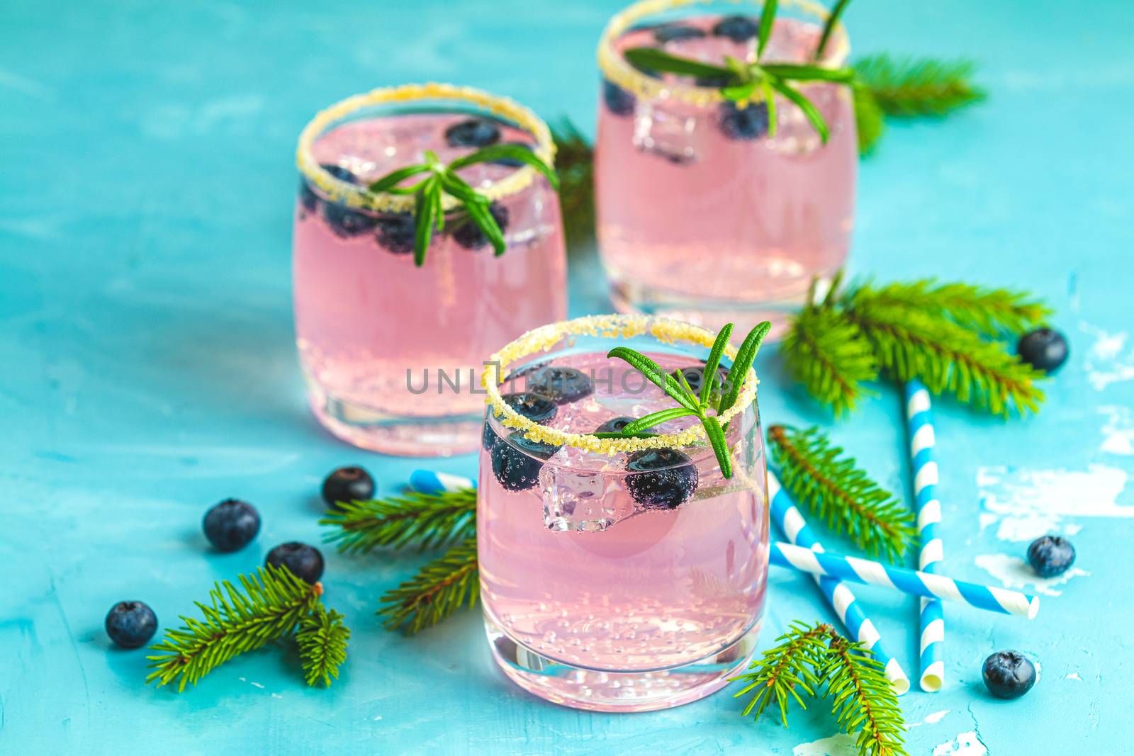 Fresh blueberry cocktail with rosemary and ice in glasses with decorate brown sugar on turquoise surface and black background. Christmas and New Year holiday welcome drink. 