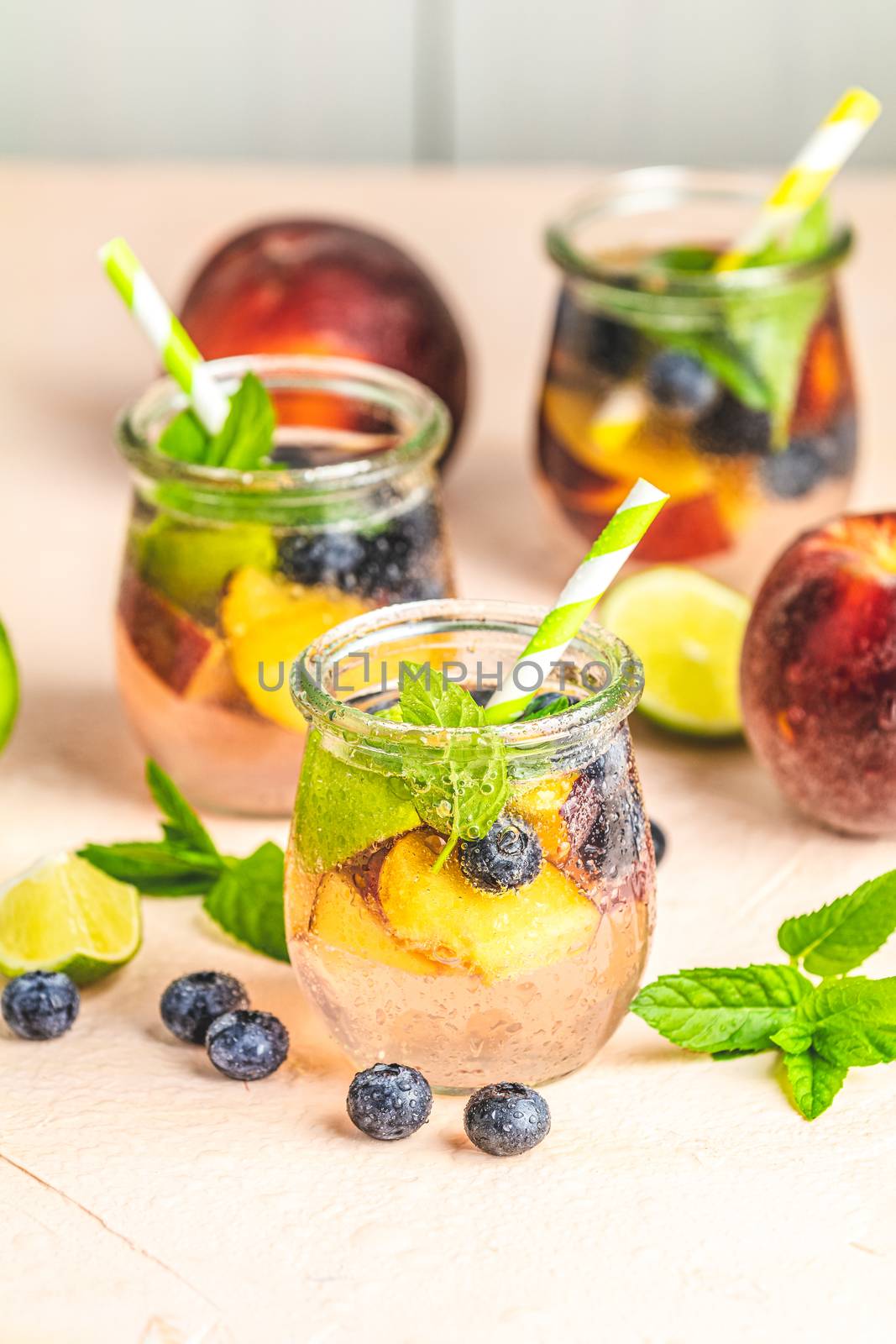 Blueberry and peach infused water, cocktail, lemonade or tea in jar with water drops. Summer iced cold drink with blueberry, lime, peach and mint