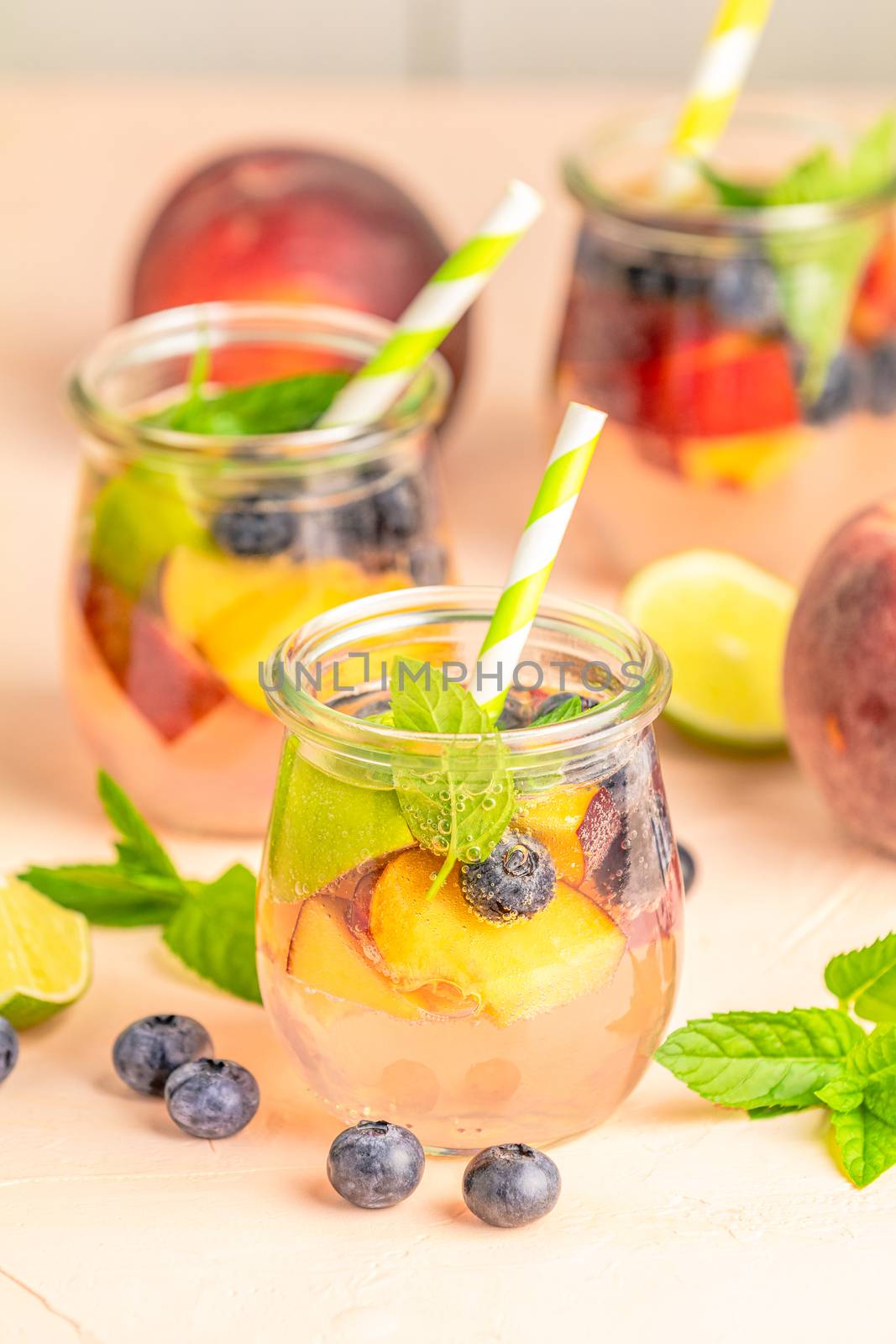 Blueberry and peach infused water, cocktail, lemonade or tea. Summer iced cold drink with blueberry, lime, peach and mint. 