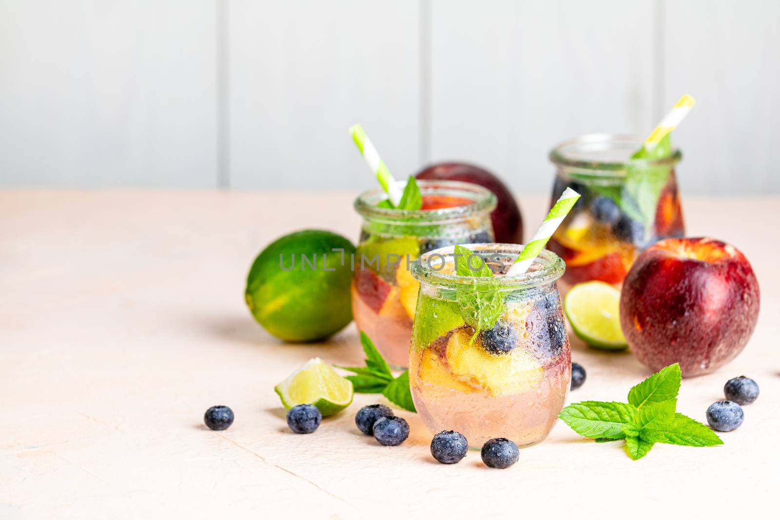 Blueberry and peach infused water, cocktail, lemonade or tea in jar with water drops. Summer iced cold drink with blueberry, lime, peach and mint