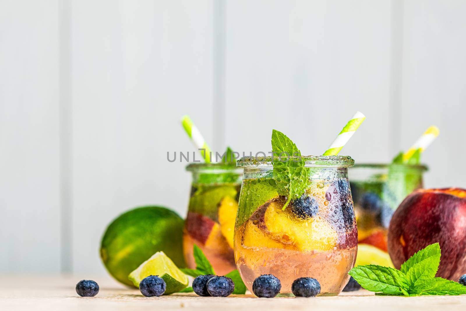 Blueberry and peach infused water, cocktail, lemonade or tea. Summer iced cold drink with blueberry, lime, peach and mint. Selective focus.
