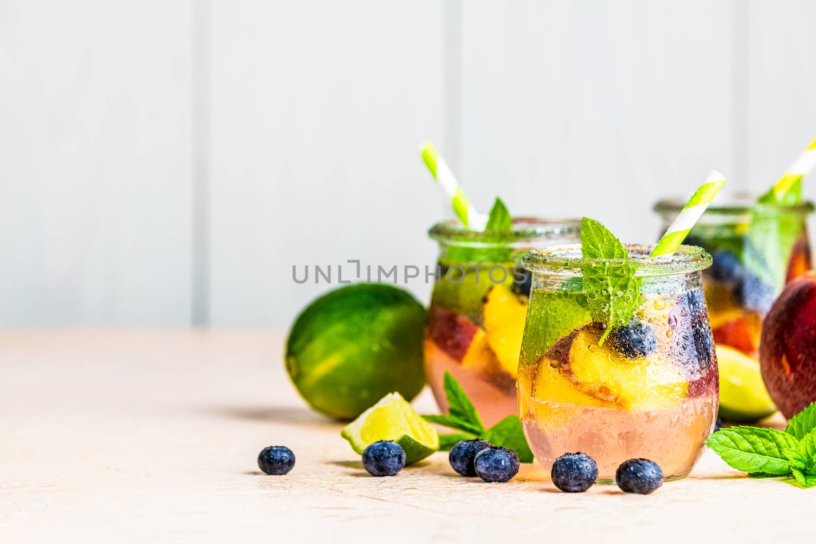 Blueberry and peach infused water, cocktail, lemonade or tea. Summer iced cold drink with blueberry, lime, peach and mint. Selective focus.