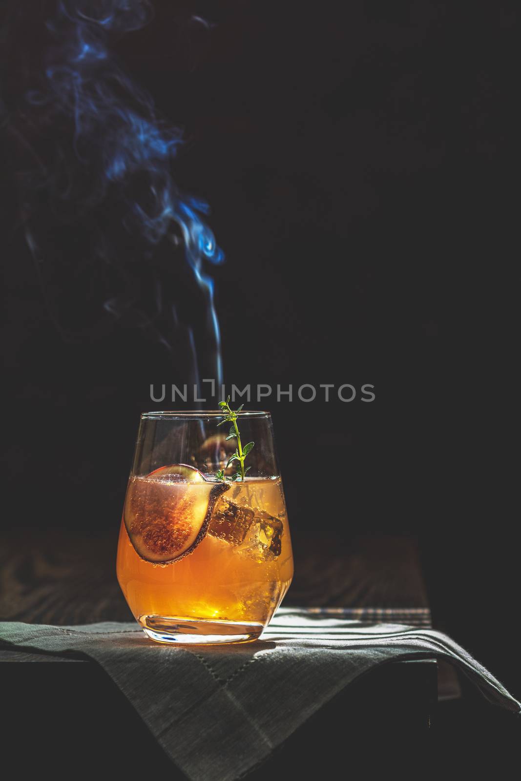 Pink cocktail with fig, thyme and ice in glass with smoke on dark wooden background, close up. Sunny light. Summer drinks and alcoholic cocktails. Alcoholic or detox cocktail