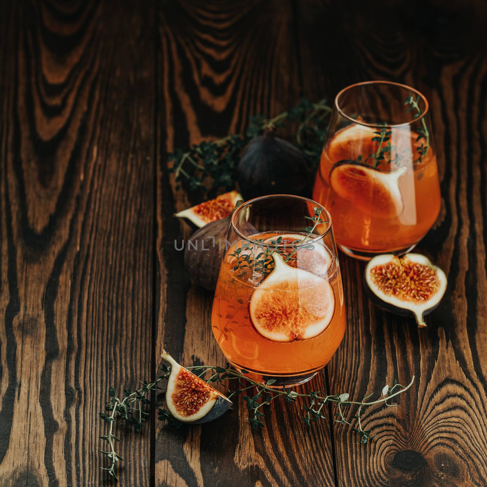 Pink cocktail with fig, thyme and ice in glass on dark wooden background, close up. Summer drinks and alcoholic cocktails. Alcoholic or detox cocktail