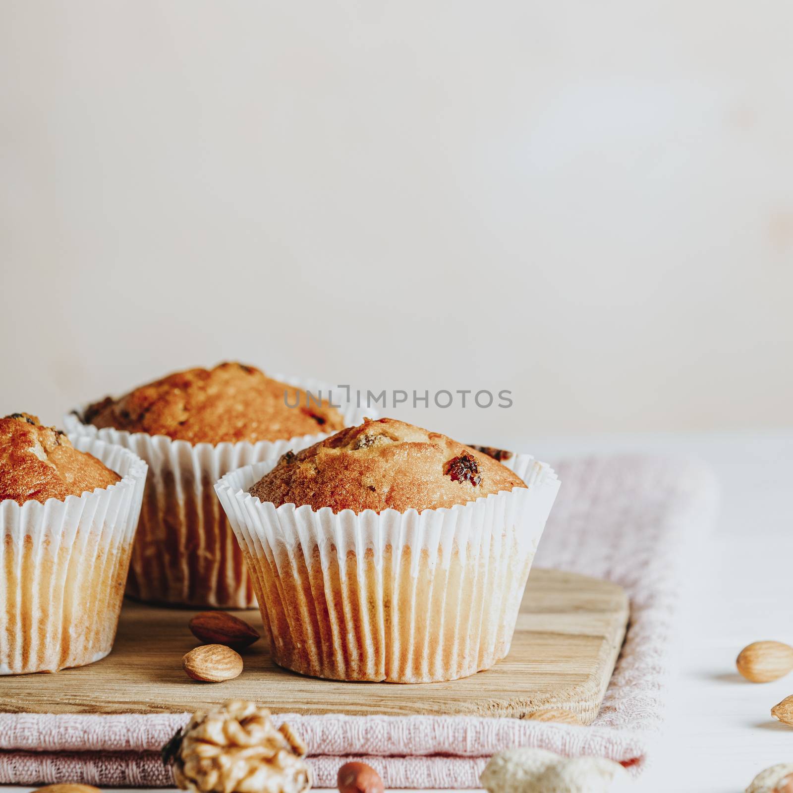 Vanilla caramel muffins in paper cups on white wooden background. Delicious cupcake with raisins, almonds and nuts. Homemade biscuit cakes. Copy space for text.