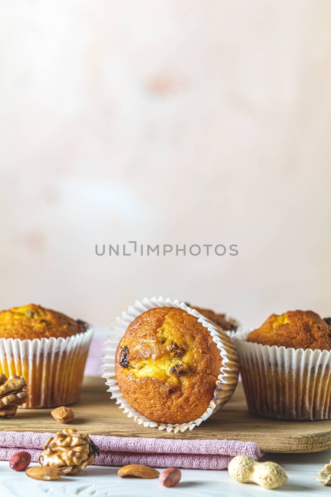 Vanilla caramel muffins in paper cups on white wooden background. Delicious cupcake with raisins, almonds and nuts. Homemade biscuit cakes. Copy space for text.