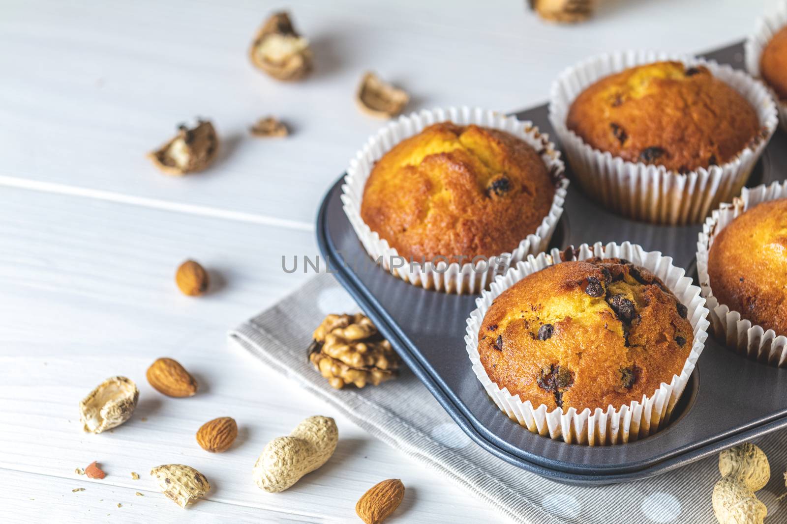 Vanilla caramel muffins in paper cups on white wooden background. Delicious cupcake with raisins, almonds and nuts. Homemade biscuit cakes. Copy space for text.