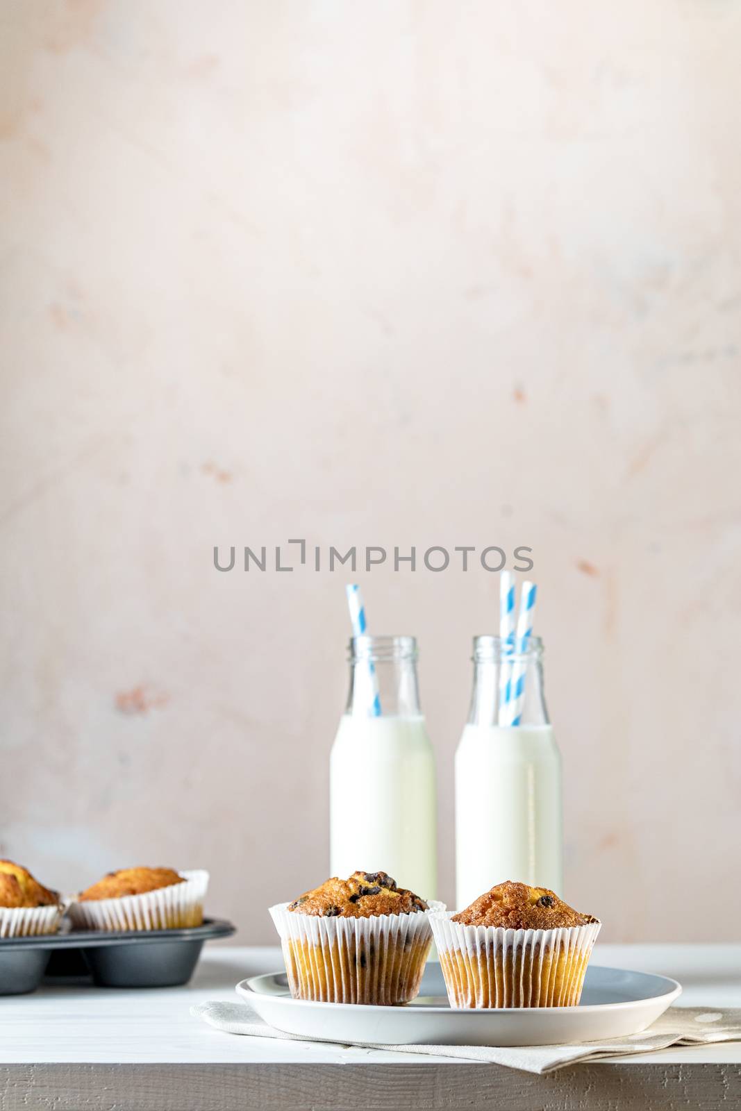 Vanilla caramel muffins in paper cups and botlles of milk on white wooden background. Delicious cupcake with raisins, almonds and nuts. Homemade biscuit cakes. Copy space for text.