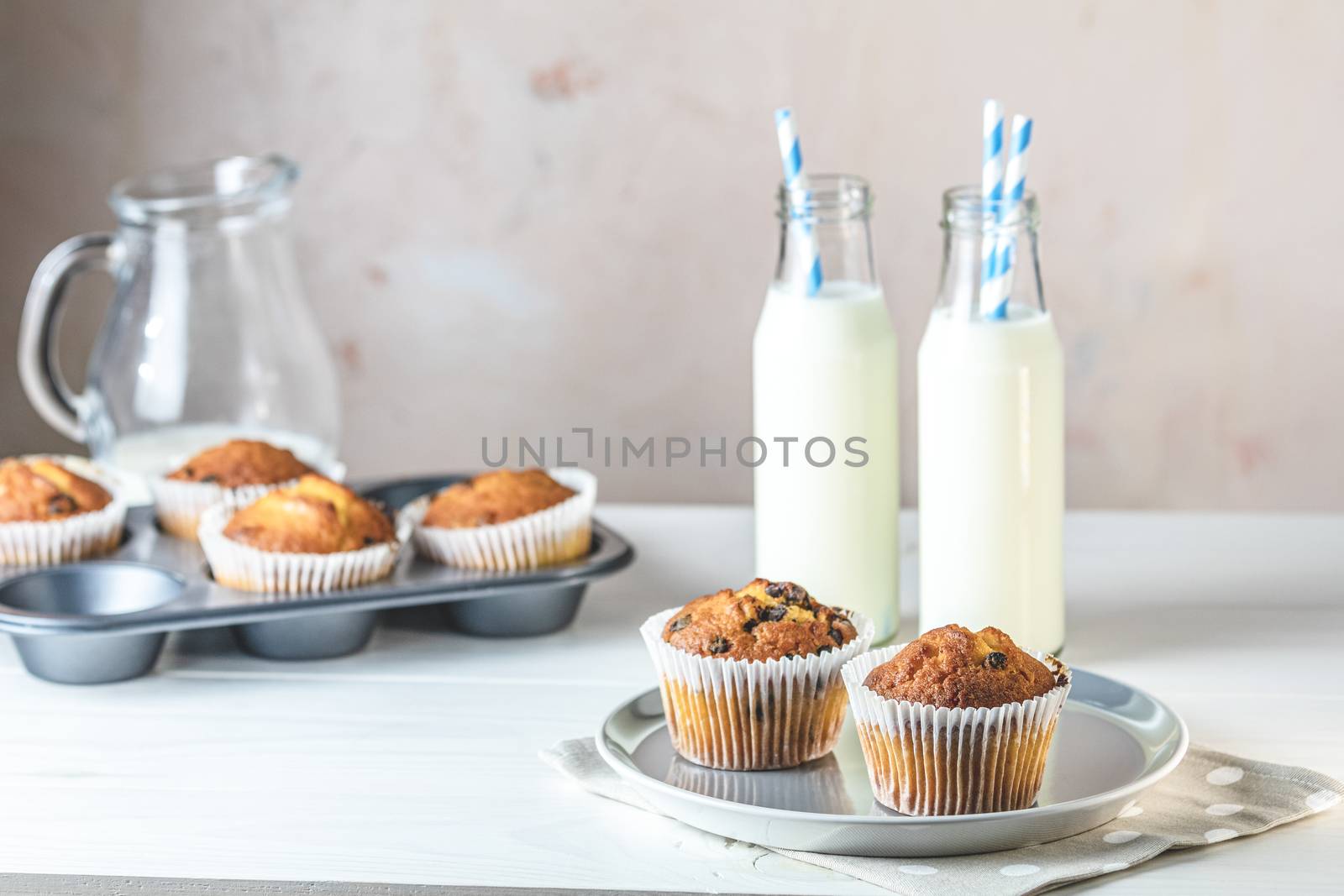 Vanilla caramel muffins in paper cups and bottles of milk on white wooden background. Delicious cupcake. Homemade biscuit cakes. Copy space for text.