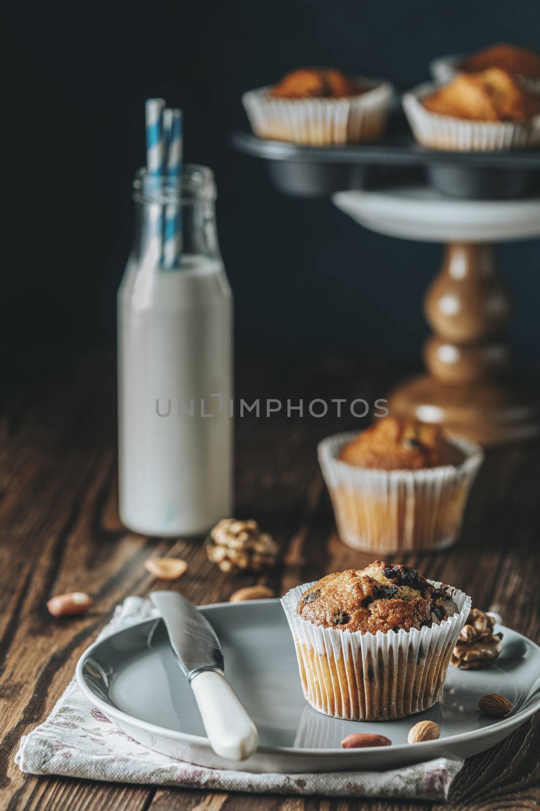 Vanilla caramel muffins in paper cups and bottles of milk on dark wooden background. Delicious cupcake with raisins, almonds and nuts. Homemade biscuit cakes. Copy space for text.