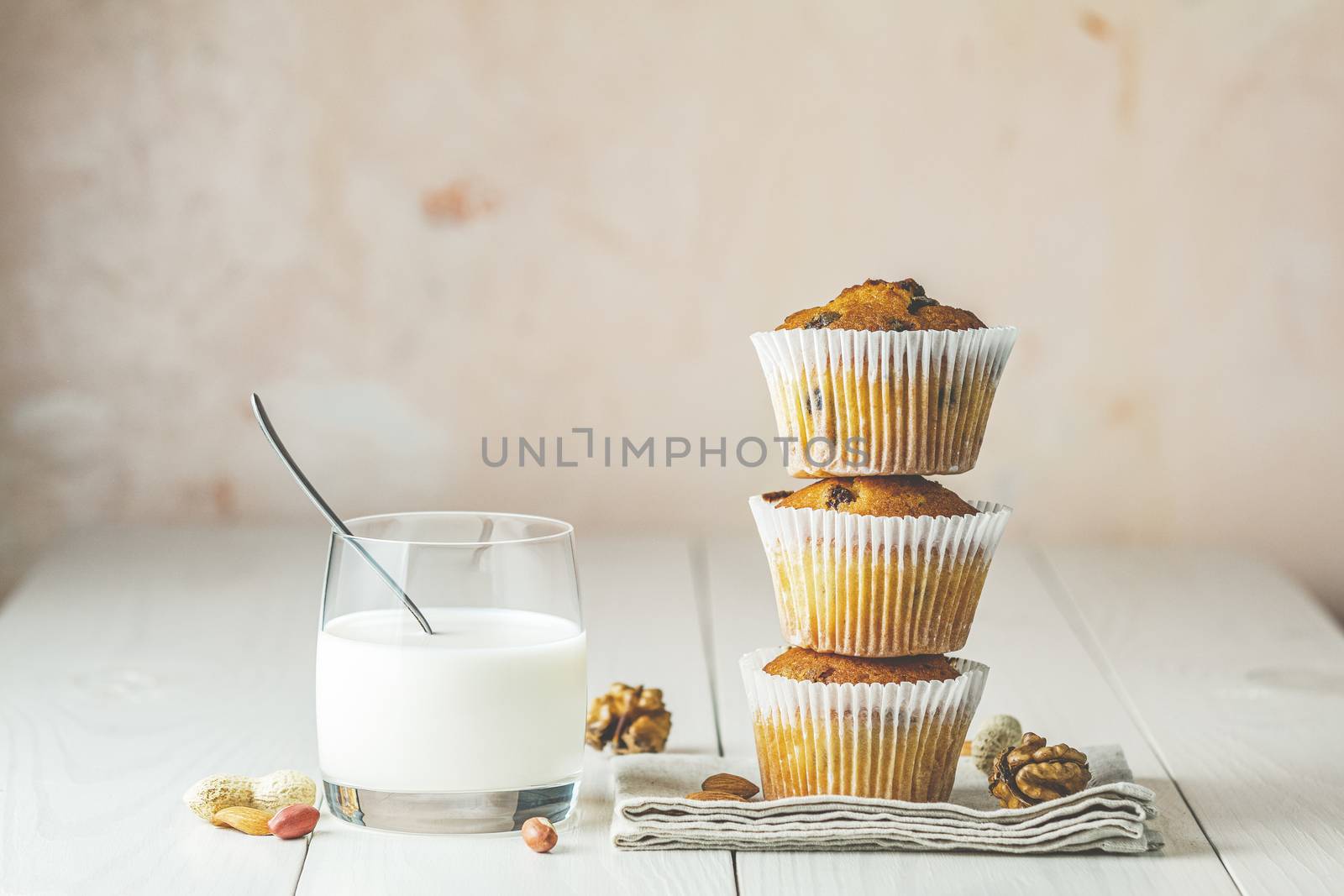 Vanilla caramel muffins in paper cups and glass of milk on white wooden background. Delicious cupcake with raisins, almonds and nuts. Homemade biscuit cakes. Copy space for text.