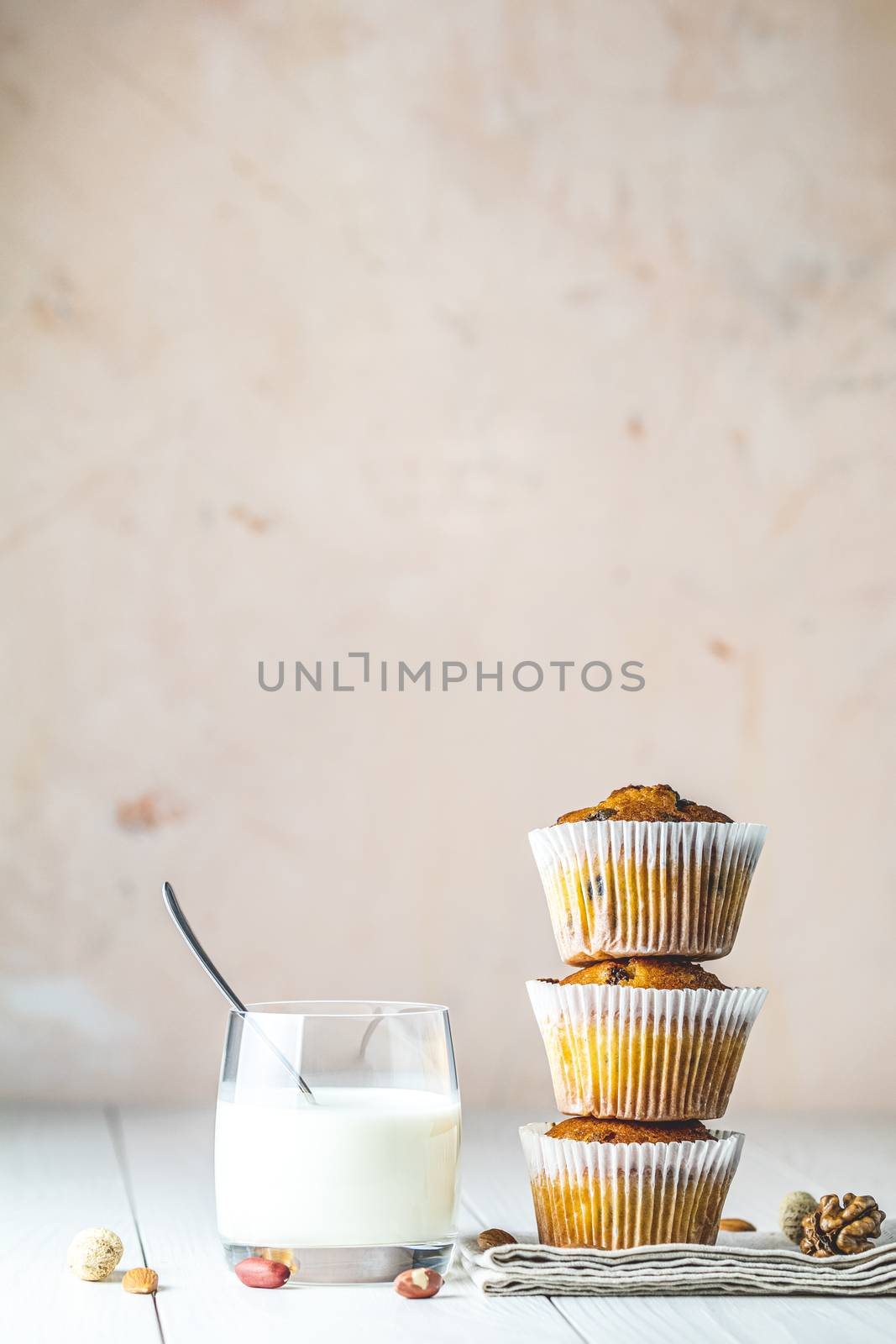 Vanilla caramel muffins in paper cups and glass of milk on white wooden background. Delicious cupcake with raisins, almonds and nuts. Homemade biscuit cakes. Copy space for text.