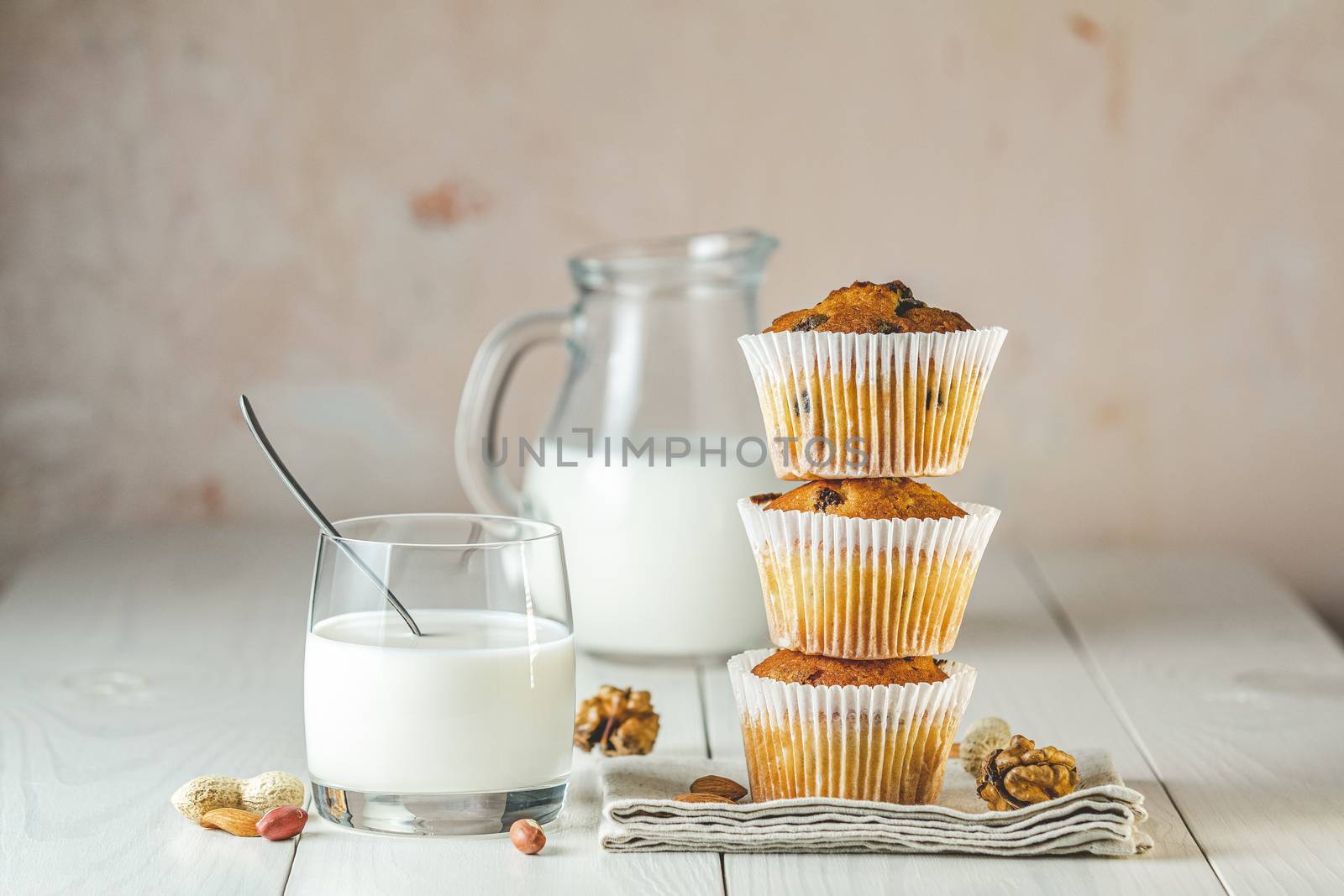 Glass of milk, vanilla caramel muffins in paper cups and bottles of milk on white wooden background. Delicious cupcake. Homemade biscuit cakes.