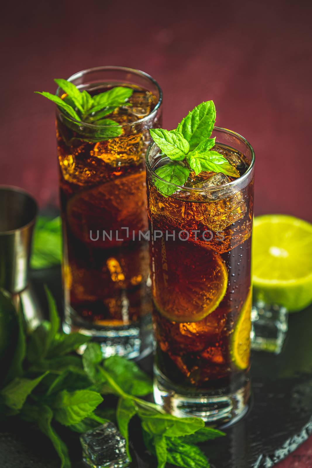 Cold Longdrink Cuba Libre with brown rum and fresh lime in highball glass with water drops on dark background, selective focus