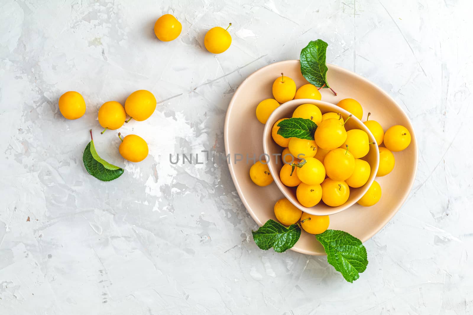 Creative summer pattern made of fresh yellow cherry plums in pink bowl on gray concrete background. Fruit minimal concept. Flat lay.