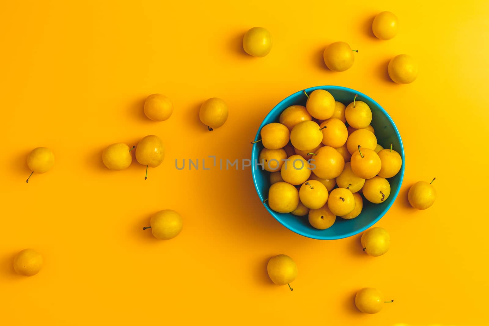 Creative summer pattern made of fresh yellow cherry plums in blue bowl on pastel yellow background. Fruit minimal concept. Flat lay.