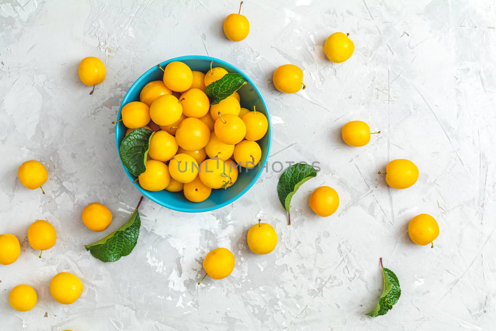 Creative summer pattern made of fresh yellow cherry plums in blue bowl on gray concrete background. Fruit minimal concept. Flat lay.