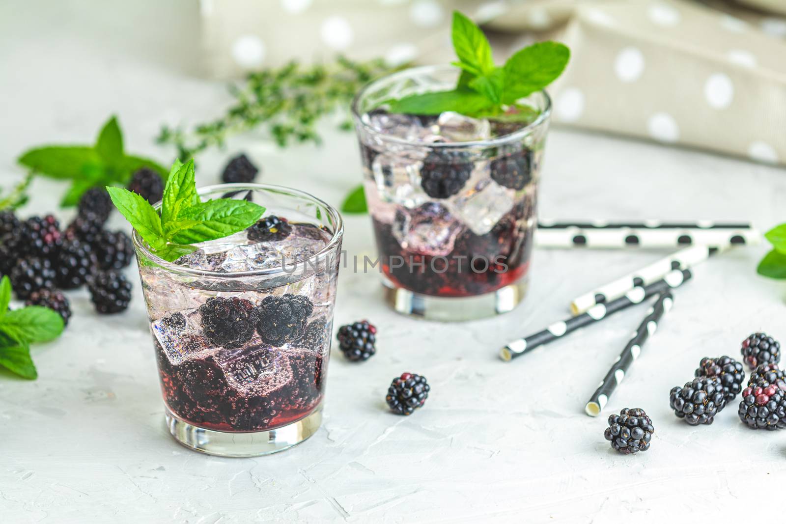 Cold summer berry drink with blackberries. Refreshing summer drink with syrup, blackberry and ice on light gray concrete background