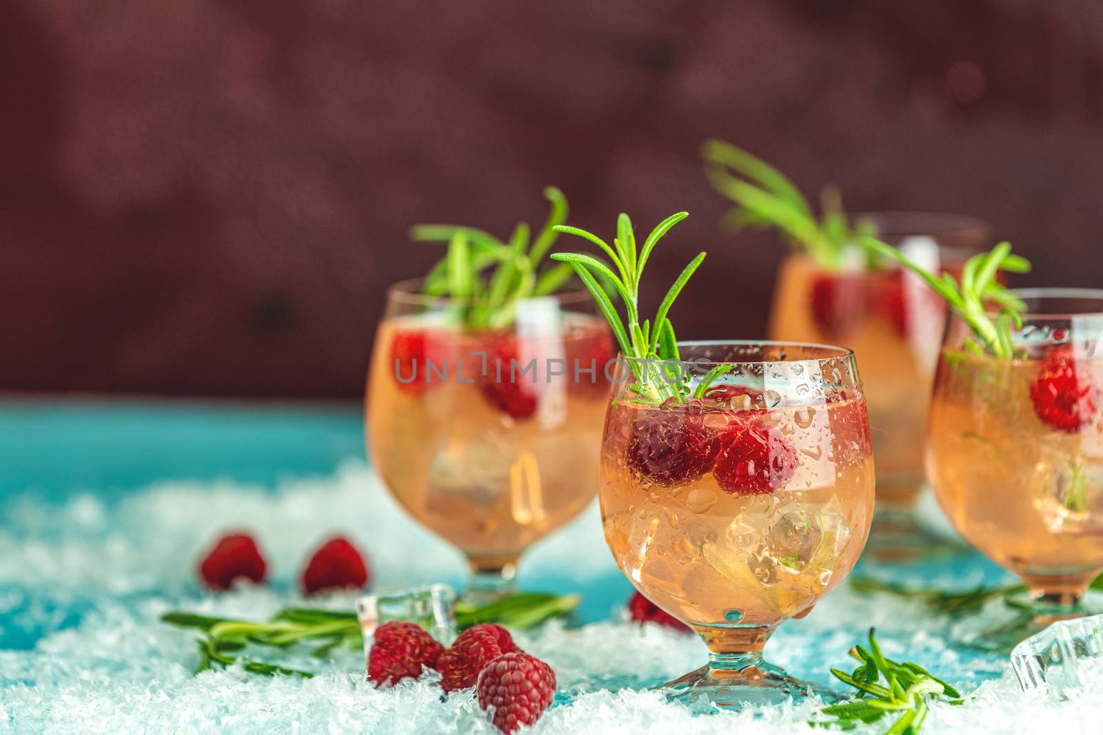 Fresh raspberry cocktail with rosemary and ice in glasses with water drops on dark background. Christmas and New Year holiday welcome drink.