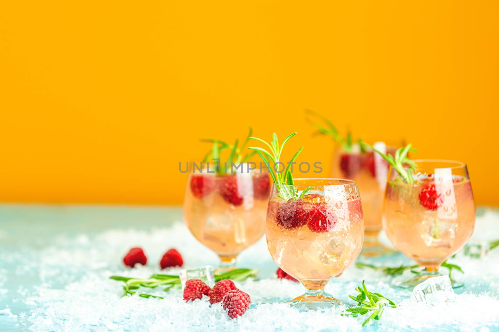 Fresh raspberry cocktail with rosemary and ice in glasses with water drops on yellow background. Christmas and New Year holiday welcome drink.