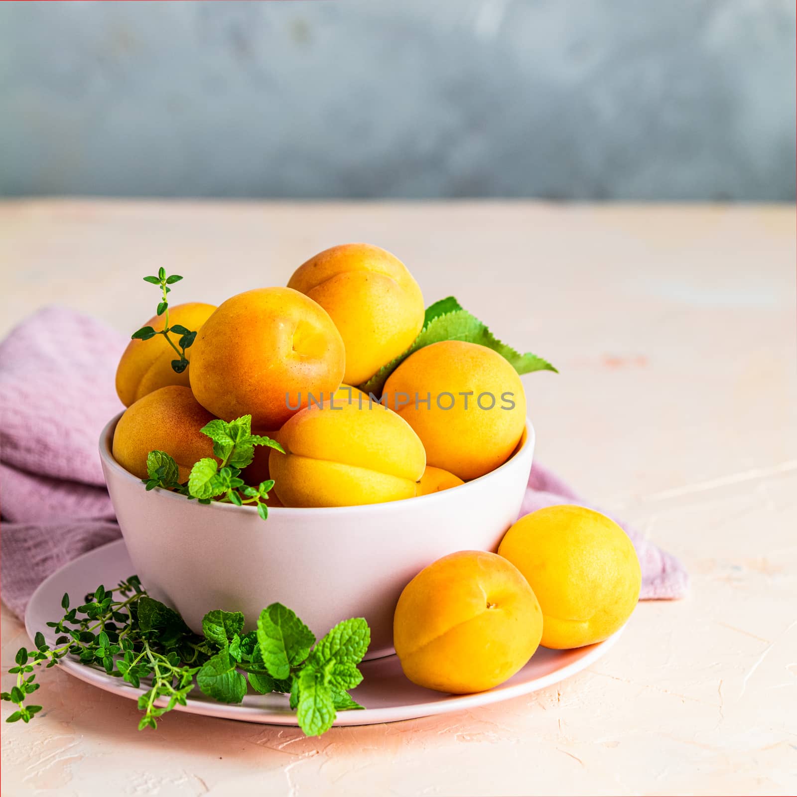 Fresh sweet orange apricots in pink bowl on the pink concrete surface table, selective focus, shallow depth of the fields