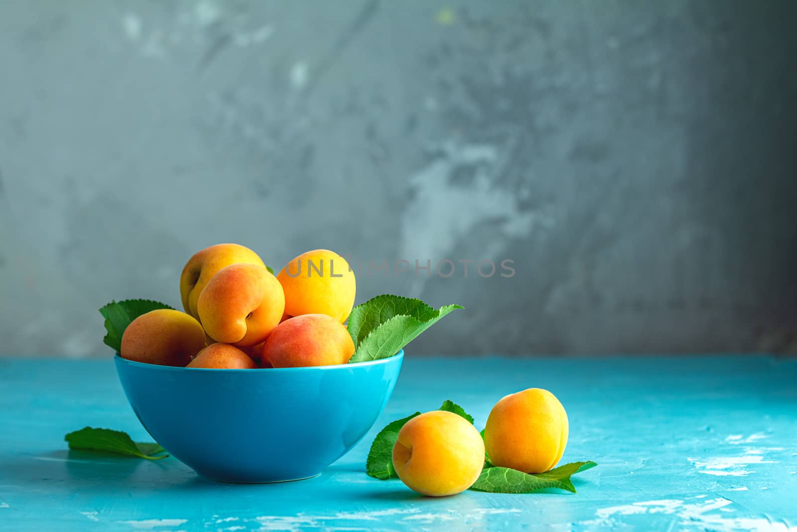 Fresh sweet orange apricots in blue bowl on the blue concrete surface table, selective focus, shallow depth of the fields