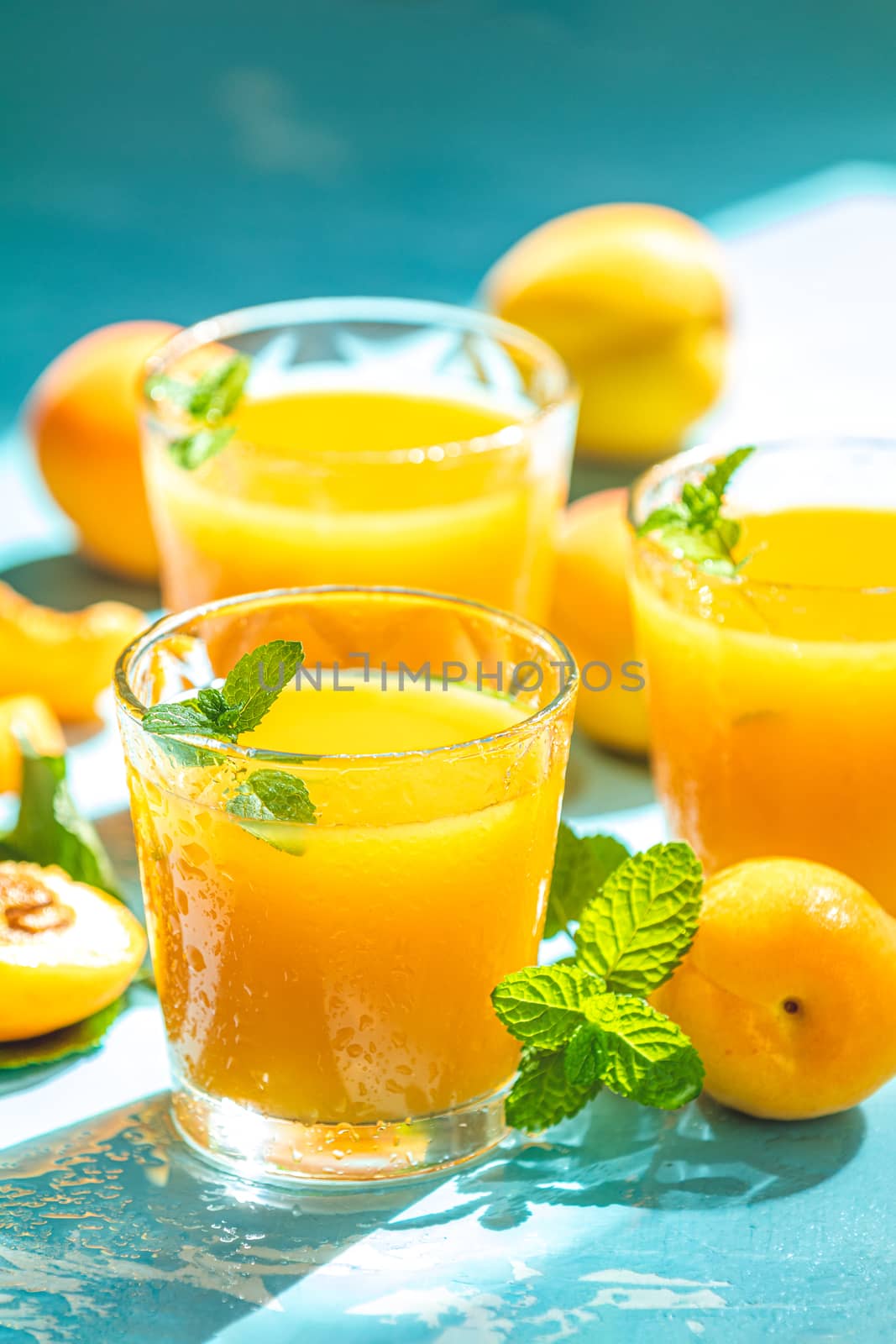 Glass of fresh healthy apricot or peach smoothie or juice on light blue concrete surface table. Sunny light. Shallow depth of the field, close up, copy space for you text