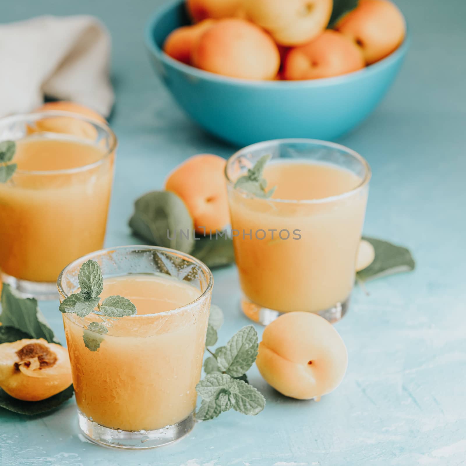 Glass of fresh healthy apricot juice in sunny light on blue surf by ArtSvitlyna