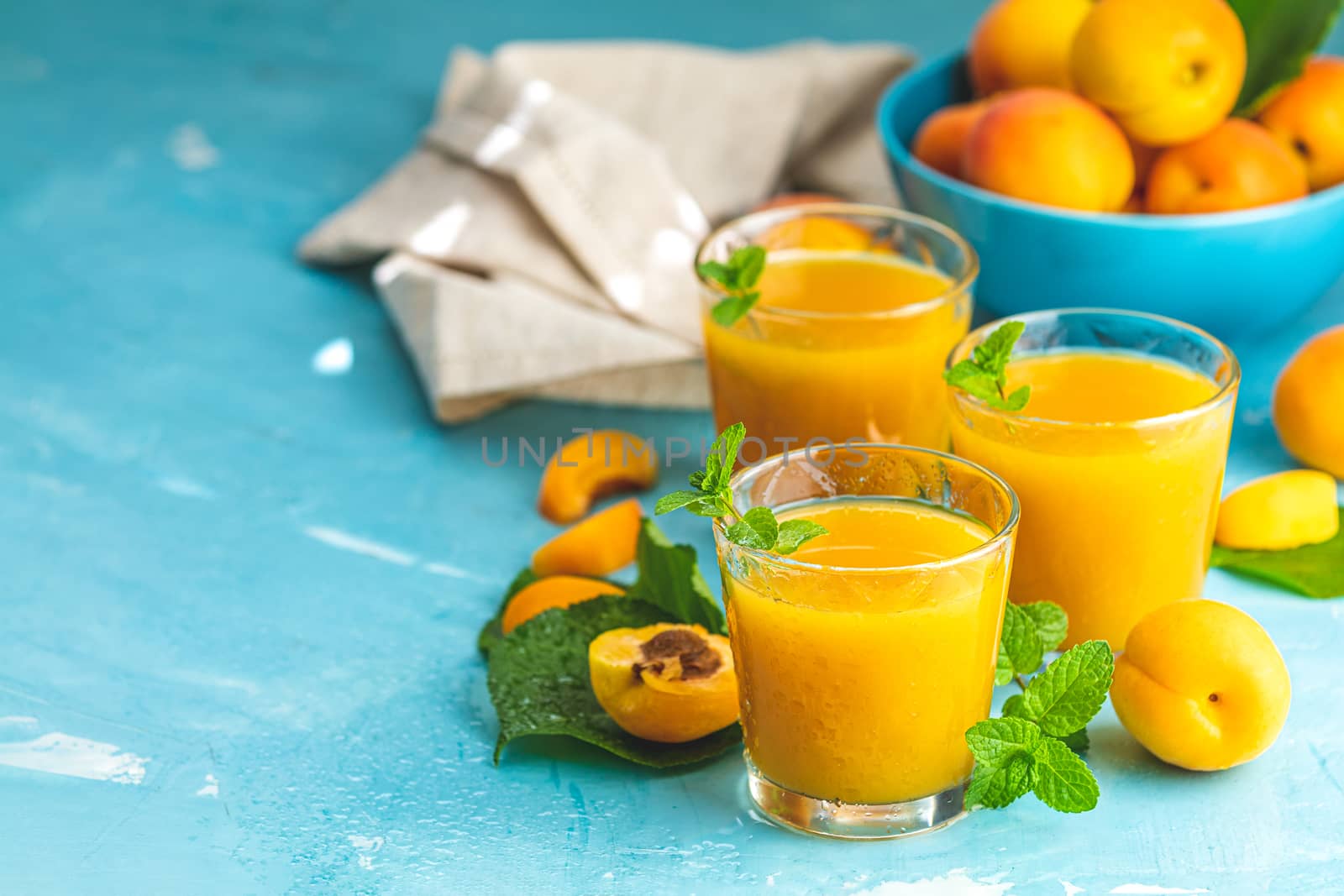 Glass of fresh healthy apricot or peach smoothie or juice on light blue concrete surface table. Sunny light. Shallow depth of the field, close up, copy space for you text