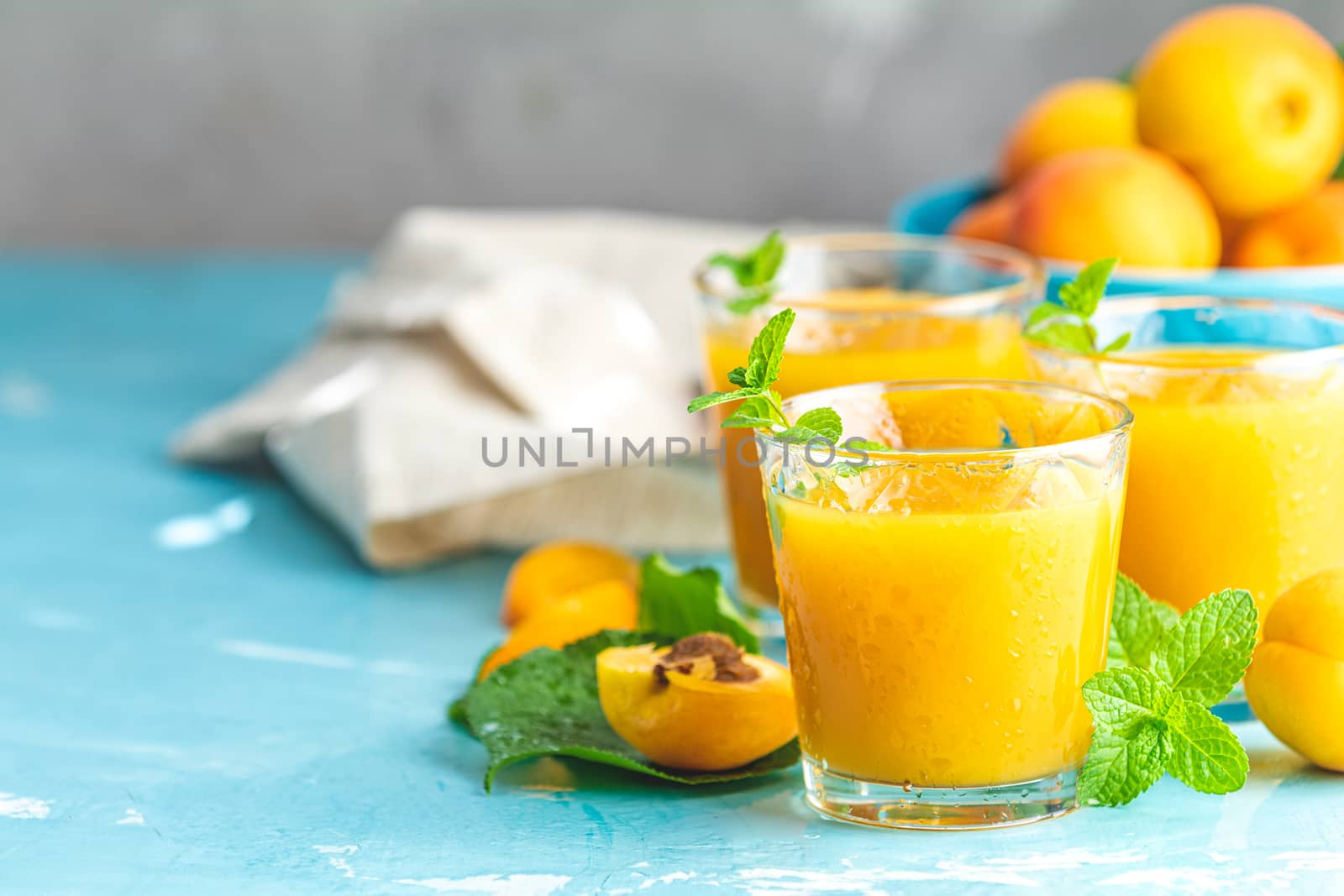 Glass of fresh healthy apricot or peach smoothie or juice on light blue concrete surface table. Sunny light. Shallow depth of the field, close up, copy space for you text