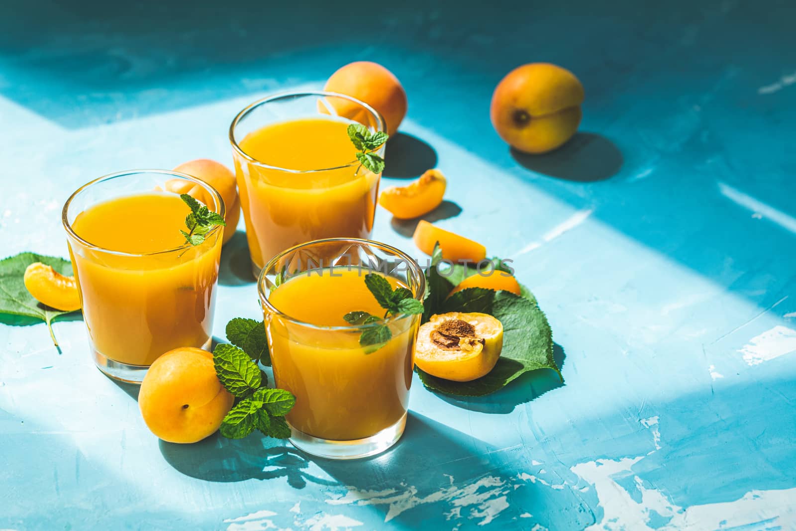 Glass of fresh healthy apricot or peach smoothie or juice on light blue concrete surface table. Sunny light. Shallow depth of the field, close up, copy space for you text