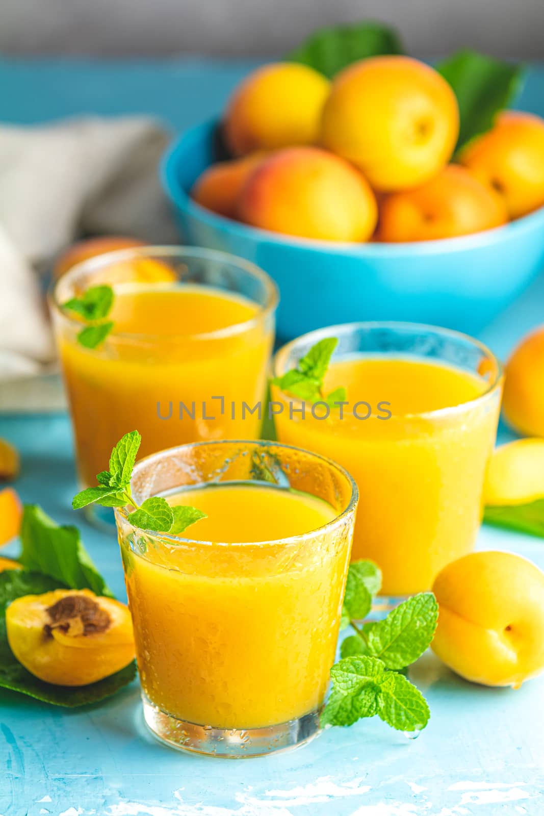Glass of fresh healthy apricot or peach smoothie or juice on light blue concrete surface table. Sunny light. Shallow depth of the field, close up, copy space for you text