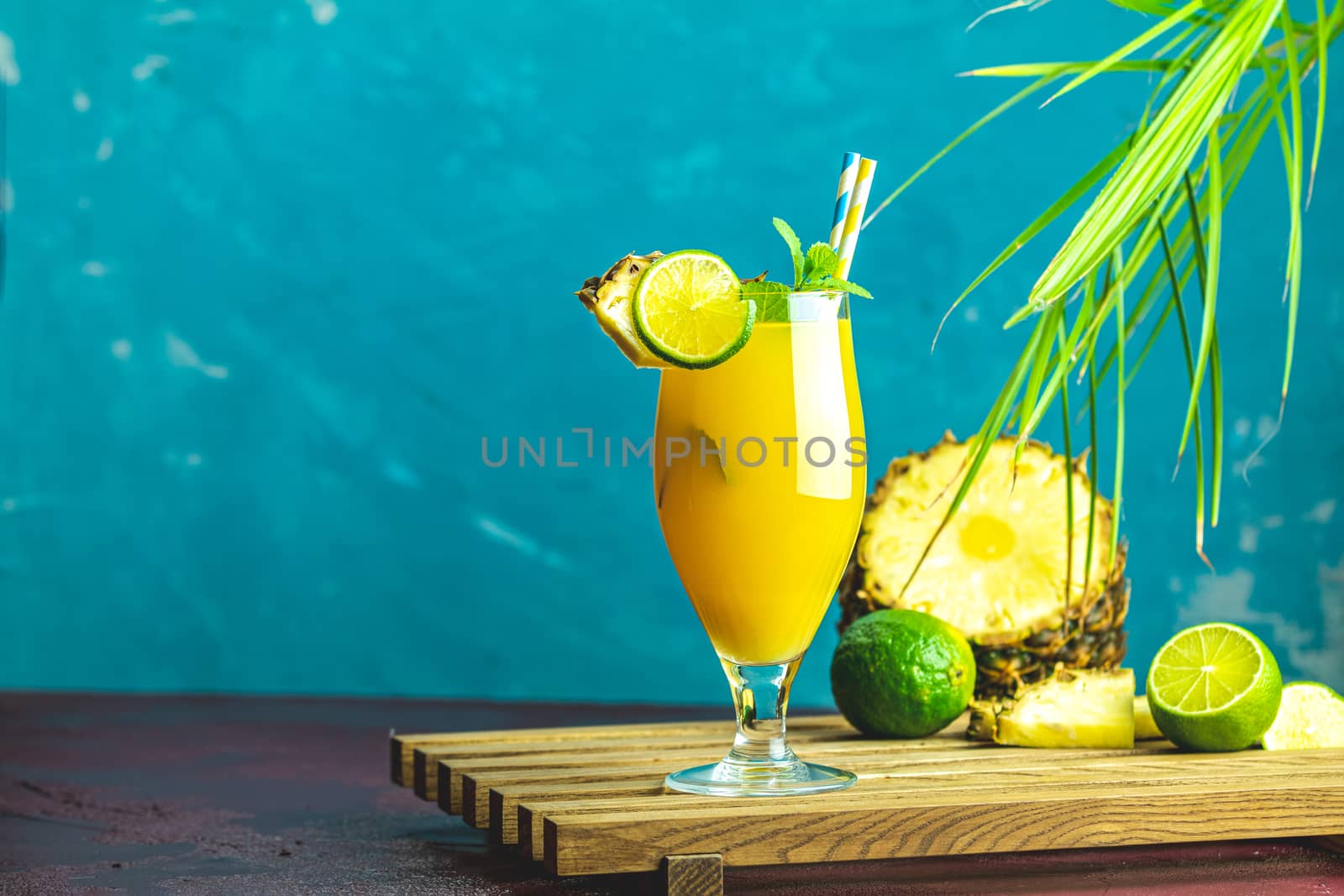 Cold cocktail with squeezed pineapple juice, lime and mint in tall glass on concrete surface table. Summer drinks and alcoholic cocktails.