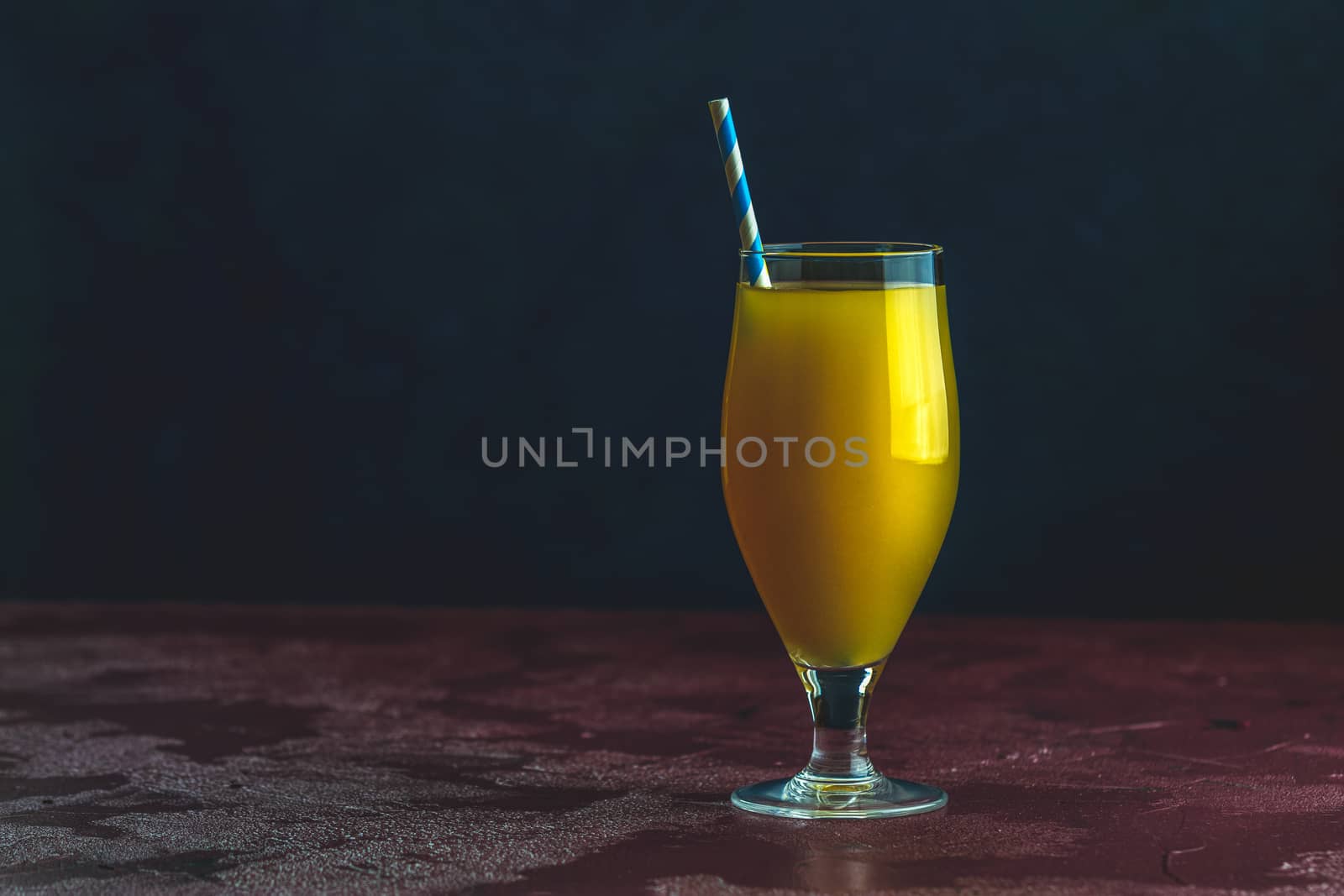 Glass of pineapple tropical fresh juice on dark bordo concrete surface table. Summer drinks and alcoholic cocktails.
