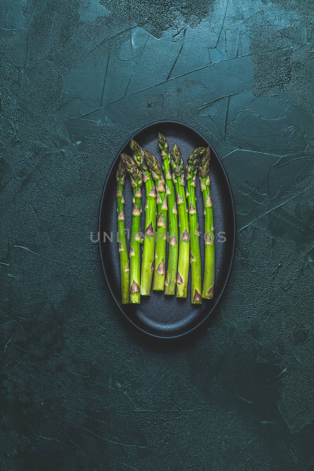 Green asparagus in  black metal pan standing on dark green concrete table background. Fresh asparagus store. Spring seasonal vegetables. Top view, copy space, flat lay.