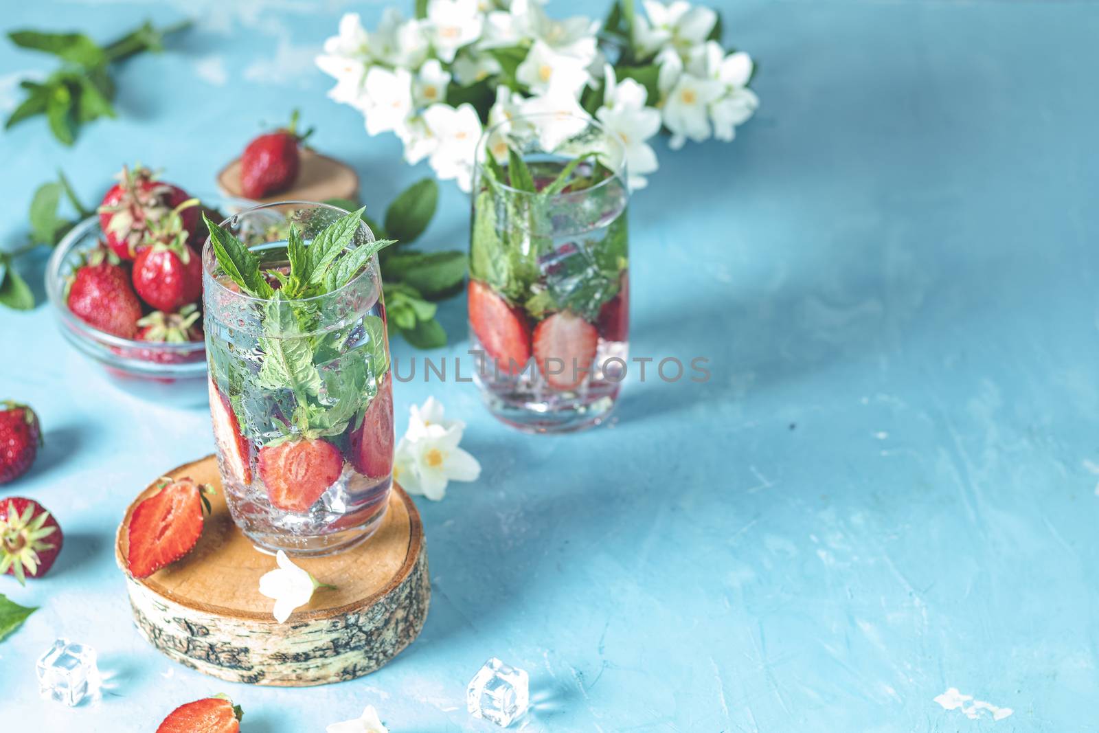 Detox infused water with strawberry and mint in highball glasses on blue concrete table background, copy space. Cold summer drink, mineral water.