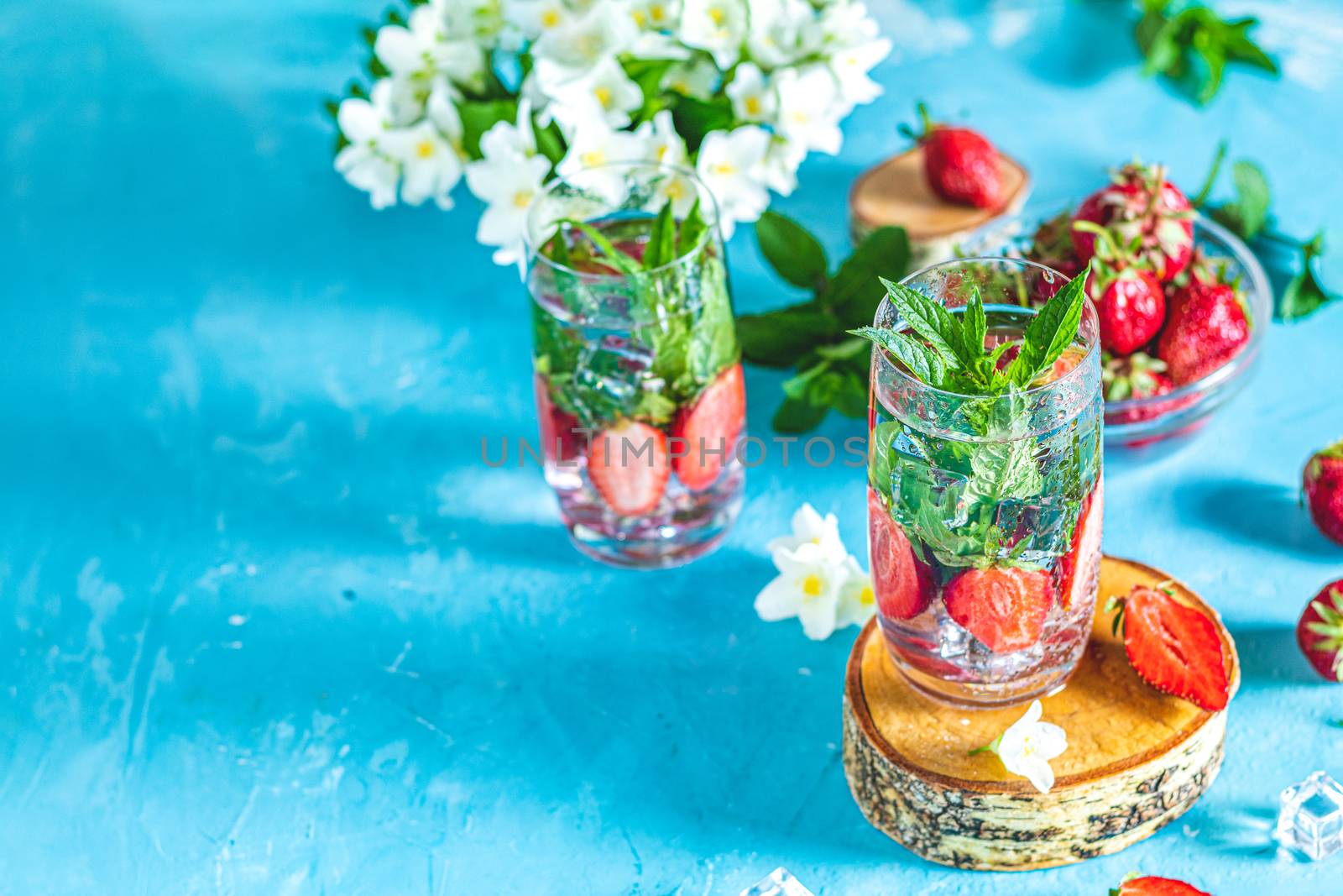 Detox infused water with strawberry and mint in highball glasses on blue concrete table background, copy space. Cold summer drink. Mineral water.