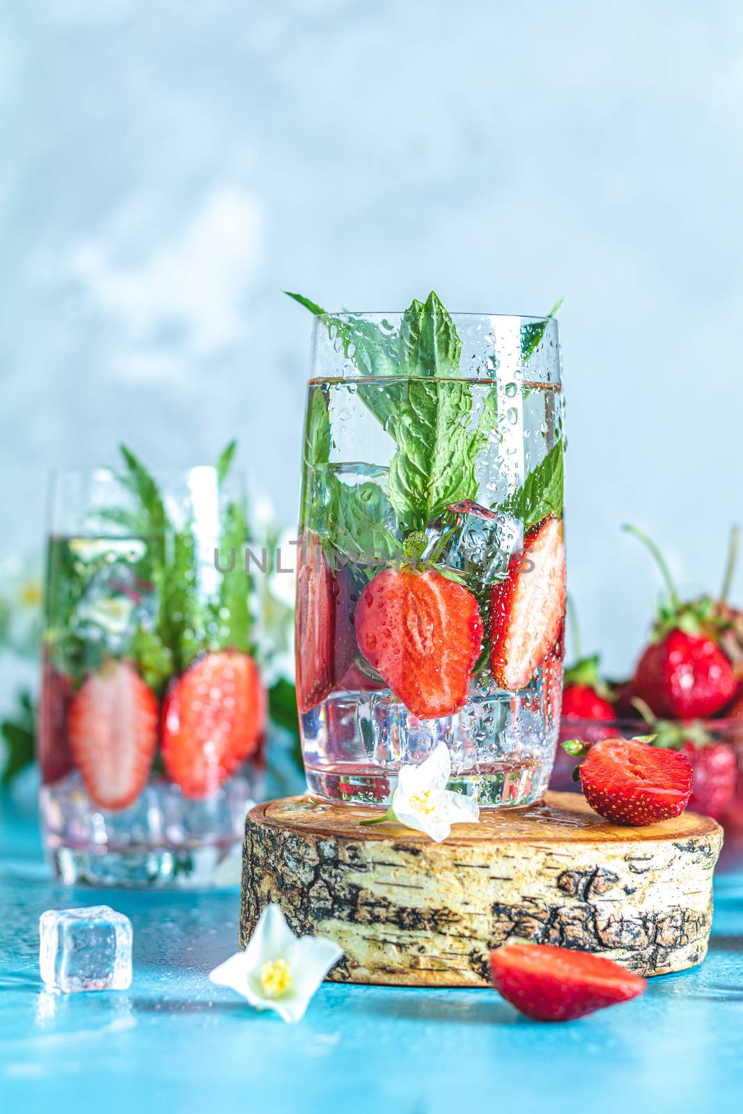 Detox infused water with strawberry and mint in highball glasses on blue concrete table background, copy space. Cold summer drink. Mineral water.