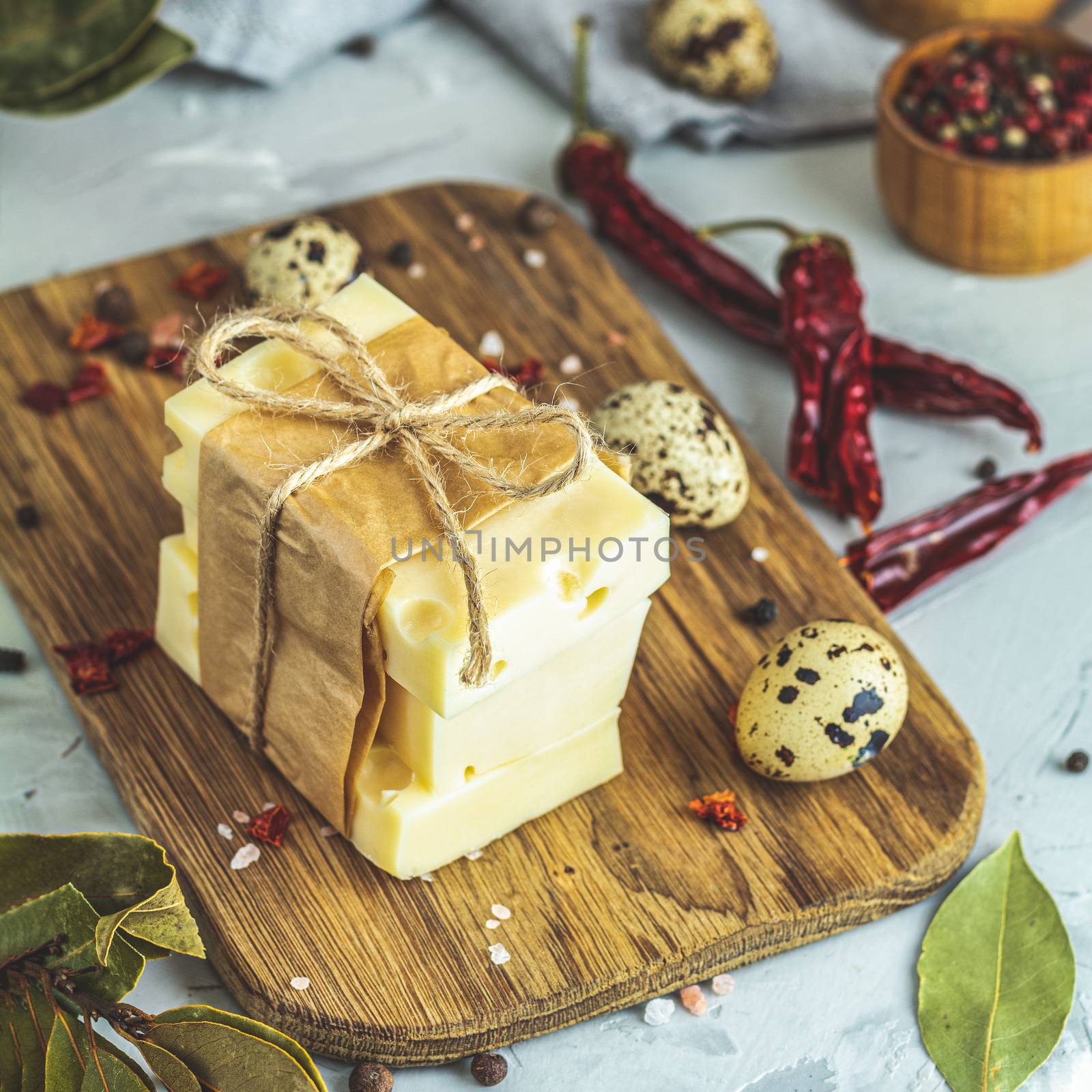 Pieces of cheese in paper on wooden board on the light gray concrete table surface. Copy space for you text.