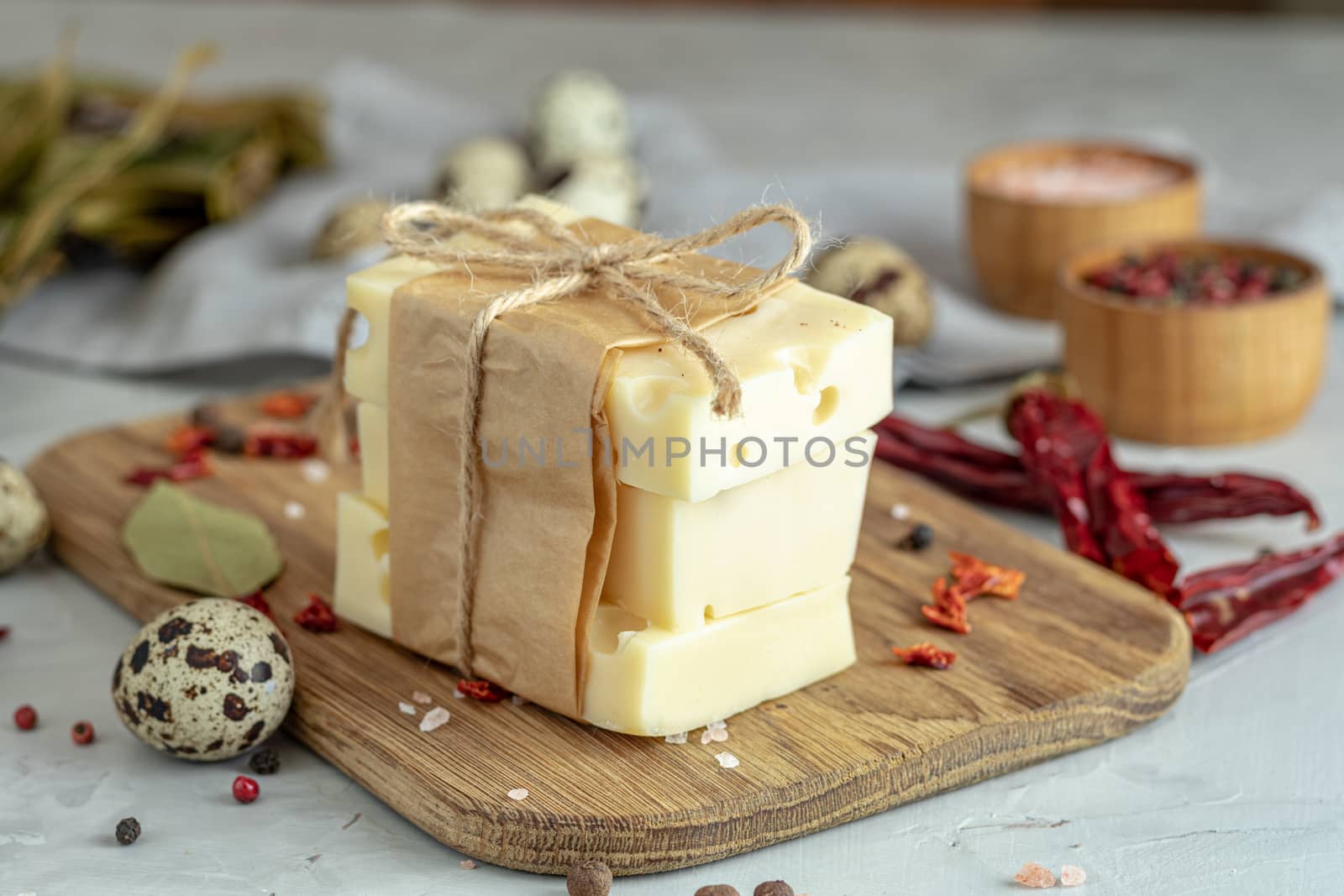 Pieces of cheese in paper on wooden board on the light gray concrete table surface. Copy space for you text.