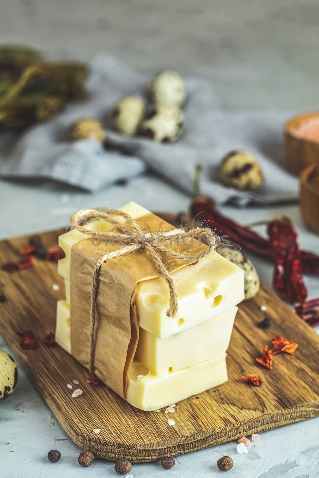 Pieces of cheese in paper on wooden board on the light gray concrete table surface. Copy space for you text.