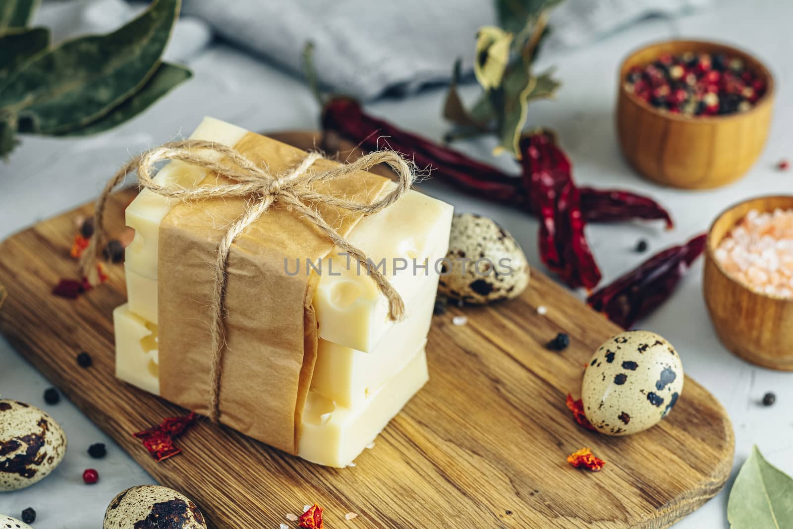 Pieces of cheese in paper on wooden board on the light gray concrete table surface. Copy space for you text.