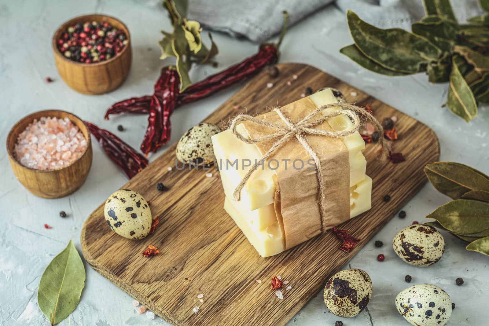Pieces of cheese in paper on wooden board on the light gray concrete table surface. Copy space for you text.