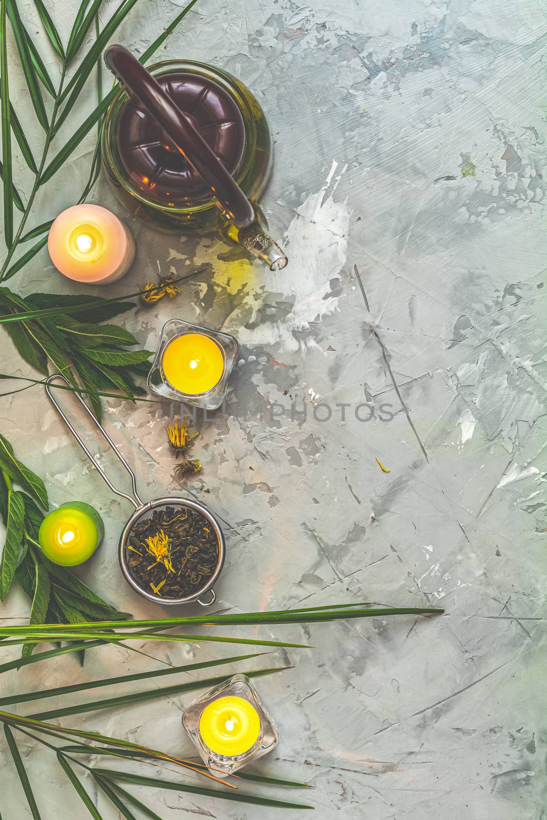 Asian tea set composition. Healthy life and relaxation concept. Glass tea pot, ceramic pot, green tea in strainer and candles on light gray concrete table background. Top view, copy space for you text