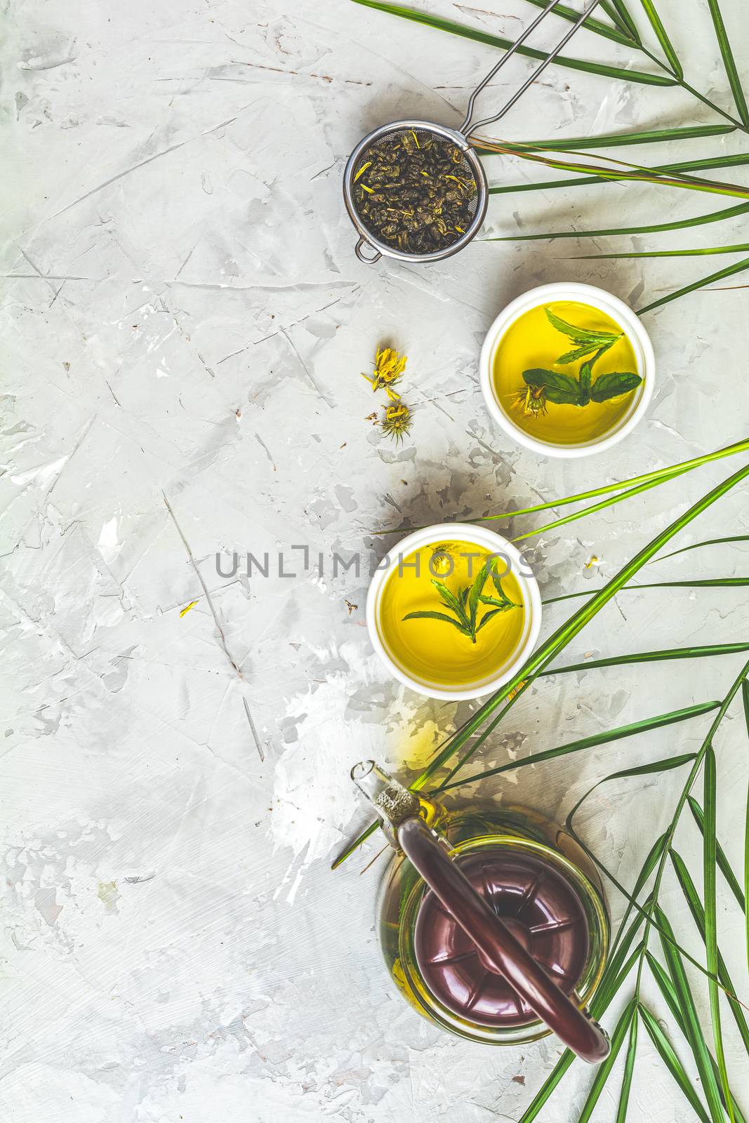 Asian tea set composition. Healthy life and relaxation concept. Glass tea pot, ceramic pot and green tea in strainer on light gray concrete table background. Top view, copy space for you text